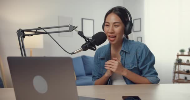 Ευτυχισμένη Ασία κορίτσι καταγράφει ένα podcast σε φορητό υπολογιστή με ακουστικά και μικρόφωνο μιλάμε με το κοινό στο σαλόνι. Γυναικείο podcaster κάνει podcast ήχου από το στούντιο του σπιτιού της. Μείνετε στο σπίτι έννοια. - Πλάνα, βίντεο