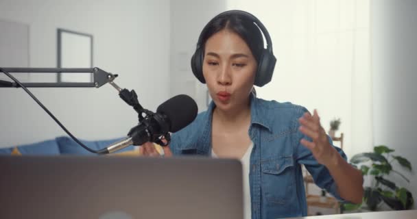 Mutlu Asyalı kız dizüstü bilgisayarda kulaklıklı bir podcast ve oturma odasında izleyicilerle mikrofon konuşması kaydediyor. Kadın podcaster kendi stüdyosundan ses yayını yapıyor. Ev konseptinde kal.. - Video, Çekim