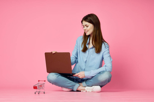 woman with laptop sitting on the floor internet communication online pink background - Фото, зображення