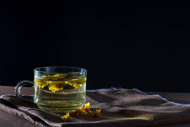 Taza de té de crisantemo con flor seca sobre mantel marrón sobre fondo negro. Bebida saludable para beber. Hierbas y concepto médico.   - Foto, imagen