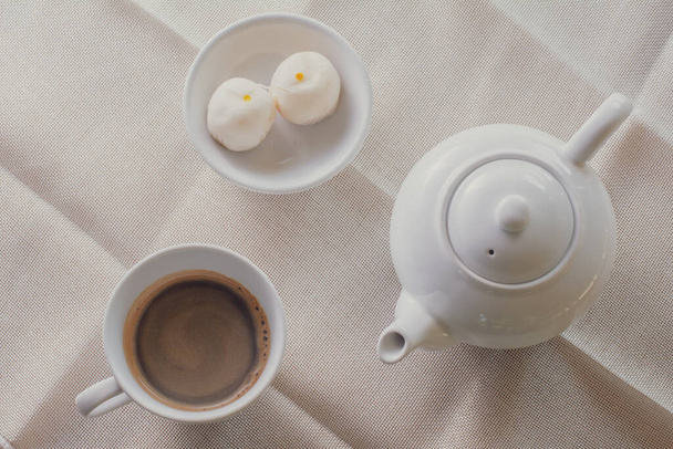 Top view white cup of hot coffee and pot served with two small mooncake on table with vintage tone. Break times concept. - Fotó, kép