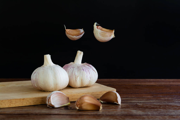 Group of garlic on chopping board and some garlic cloves floating in the air on wooden table with black background. Copy space for your text. - Photo, Image