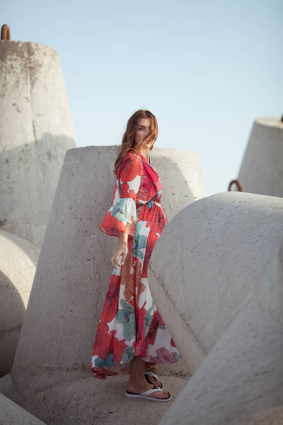 Beautiful woman in a long red dress near breakwater, a walk by the sea - Photo, Image
