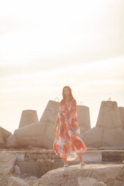 Beautiful woman in a long red dress near breakwater, a walk by the sea - Photo, image