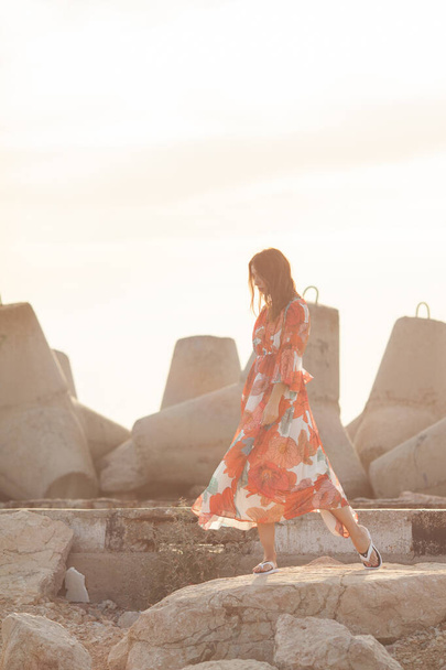 Beautiful woman in a long red dress near breakwater, a walk by the sea - Photo, image