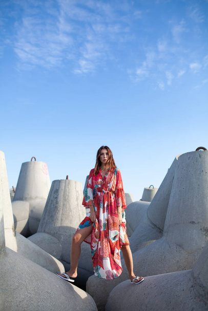 Beautiful woman in a long red dress near breakwater, a walk by the sea - Fotó, kép