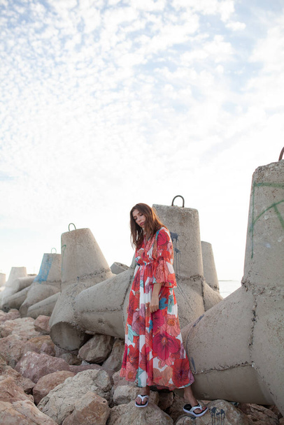 Beautiful woman in a long red dress near breakwater, a walk by the sea - Фото, изображение