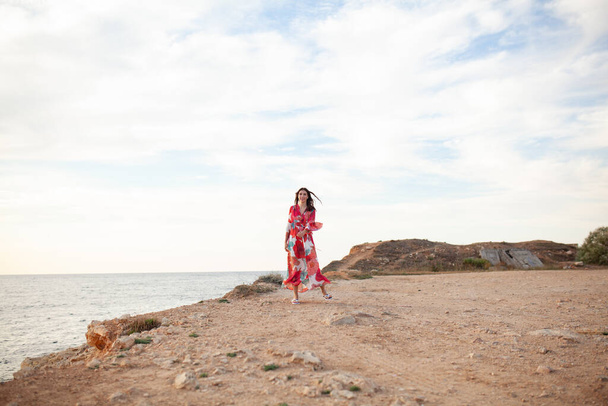Beautiful woman in a long red dress near sea, a walk by the shore - Photo, image
