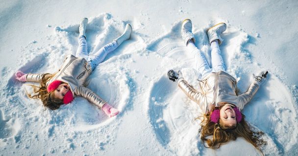Twee kleine meisjes die sneeuwengel maken terwijl ze op sneeuw liggen. gelukkig kinderen meisjes op een sneeuw engel shows. - Foto, afbeelding