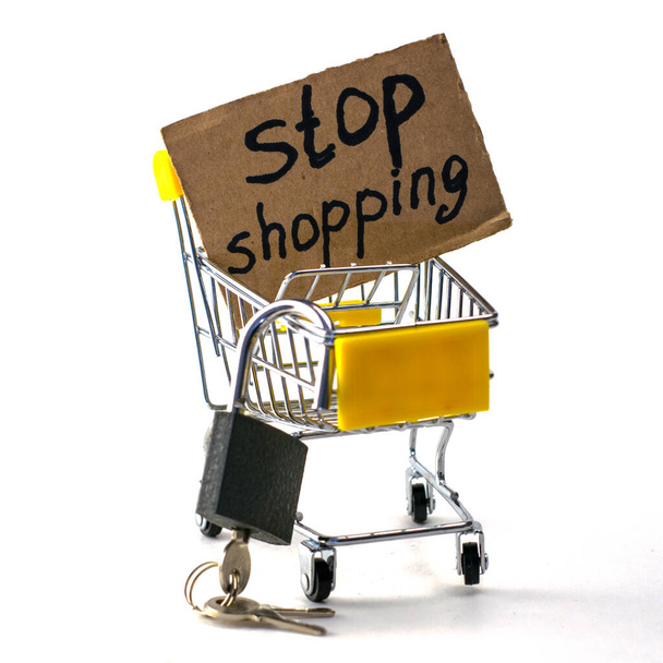 the concept of refusing to buy a reasonable consumption shopping cart with a padlock and a sign saying stop shopping on a white background. High quality photo - Photo, Image