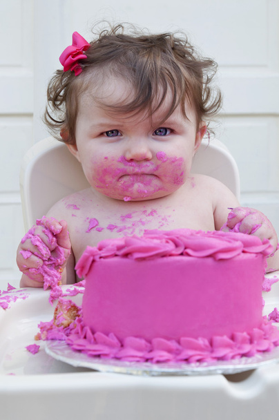 Baby girl eating first birthday cake with pink frosting and bow in her hair - Photo, image