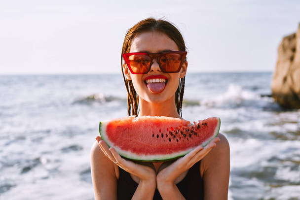 весела жінка в сонцезахисних окулярах їсть кавун біля океану
 - Фото, зображення