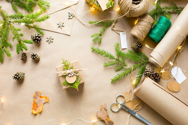 Pack a gift for Christmas and new year in eco-friendly materials: kraft paper, live fir branches, cones, twine. Tags with mock up, natural decor, hand made, DIY. Festive mood. Flatly, background - Foto, Imagen