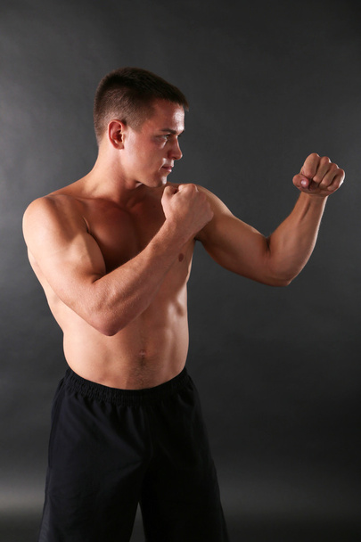 Handsome young muscular sportsman boxing on dark background - 写真・画像
