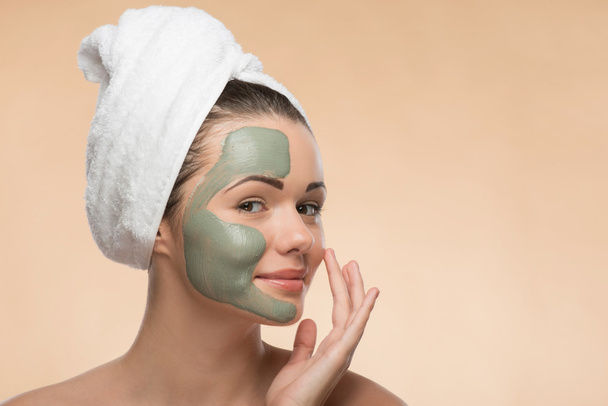 Spa girl with a  towel on her head applying facial clay mask and - Foto, Imagem
