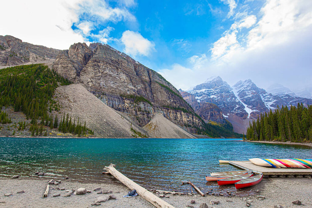 Several boats and canoes are moored on the shore of the mountain lake Moraine.The magnificent Canadian Rockies are covered with glaciers. Banff Park. Travel to northern Canada - Fotoğraf, Görsel