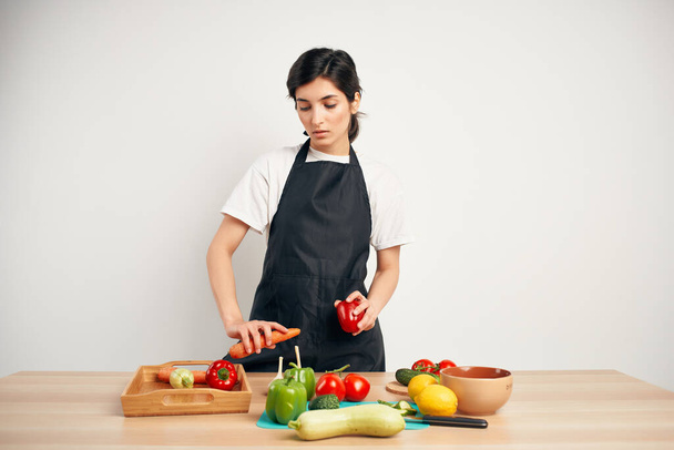 dona de casa em um avental preto na cozinha cortando legumes alimentação saudável - Foto, Imagem