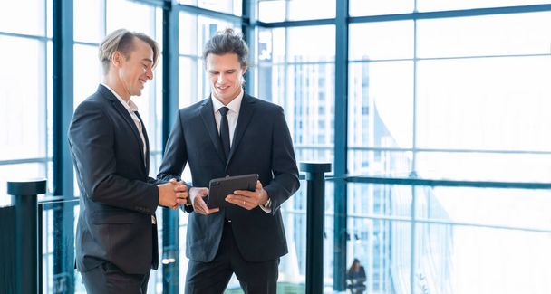 Καυκάσιος επιχειρηματίας με επίσημη στολή συζητά μαζί ενώ εργάζεται στο σύγχρονο κτίριο χρησιμοποιώντας ψηφιακή ταμπλέτα - Φωτογραφία, εικόνα