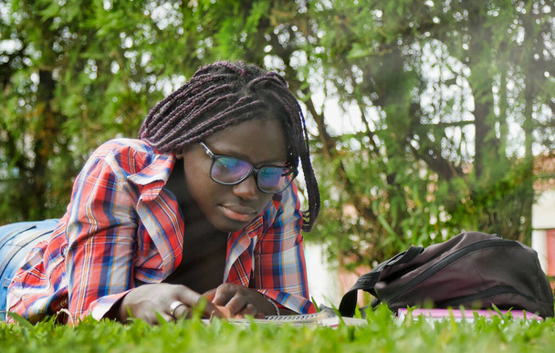Африканська дівчинка - підліток лежить на траві і робить уроки в школі. Концепція щасливості і живучості. - Фото, зображення