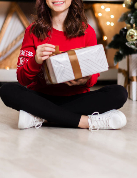 Girl in a red sweater and jeans posing with a New Year gift in her hands - Foto, imagen