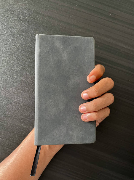 Notitieboek in de hand. een klein grijs notitieboekje om alles op te nemen, inclusief ideeën en essentiële dingen. gesloten notebook met divider. - Foto, afbeelding