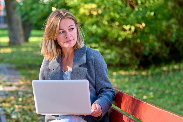 Una donna con un computer portatile è seduta su una panchina del parco - Foto, immagini