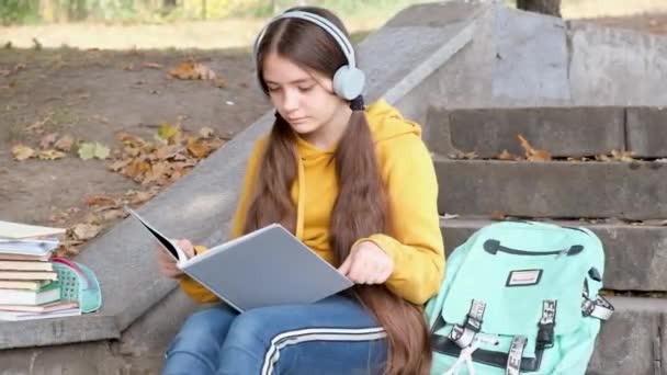 Een meisje van 13 jaar oud zit op de trap en leest een boek in het park, gaat naar school examens. - Video
