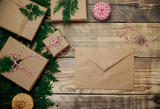 Boxes packed in kraft paper and green branches on a wooden background. An envelope, a letter of congratulations. Environmentally friendly material.Christmas and New Year. - Zdjęcie, obraz
