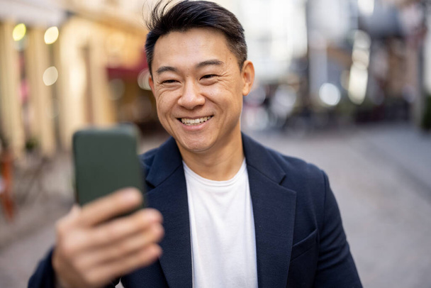 Asiatico uomo holding smartphone e guardando macchina fotografica - Foto, immagini