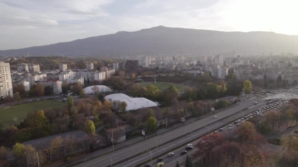Sofia cityscape fő utcai dugó naplementekor. Futballpályák és zöld parkok az üzleti negyedben - Felvétel, videó
