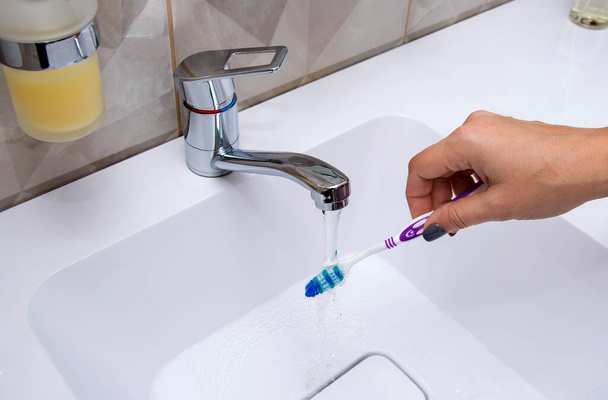A woman's hand holding a toothbrush and toothpaste under running water from the tap - Foto, Imagem