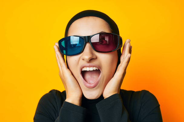 Muslim in black hijab popcorn 3D glasses cinema yellow background - Foto, Imagen