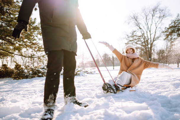 Счастливая женщина катается на санках в зимнем заснеженном лесу. Пара весело провести время в зимней природе. Отдых, отдых, концепция путешествий. - Фото, изображение