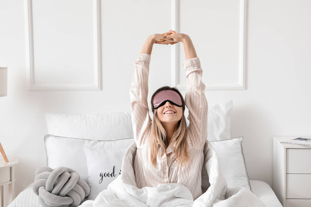 Νεαρή γυναίκα με μάσκα ύπνου που τεντώνεται στο κρεβάτι - Φωτογραφία, εικόνα