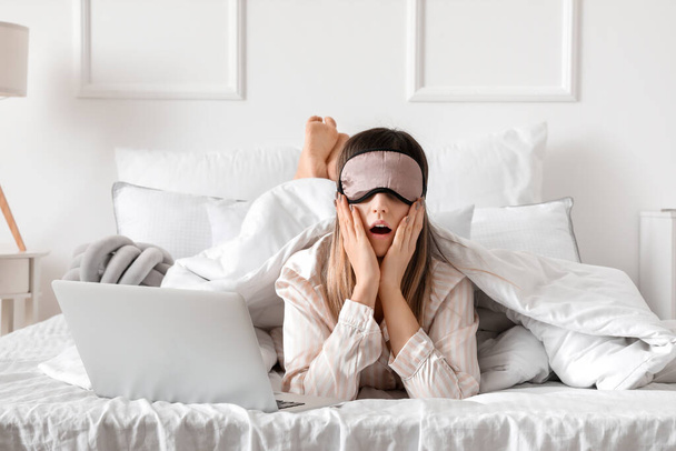 ベッドの上に寝そべっているマスクとラップトップを持つショックを受けた女性 - 写真・画像