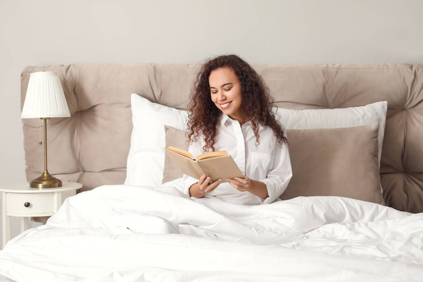 Morning of young woman reading book in bed - 写真・画像