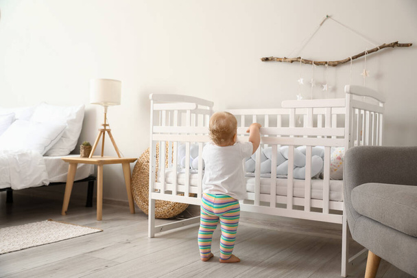 Adorable little baby standing near crib at home - Valokuva, kuva