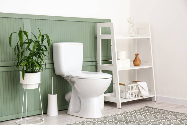 Bol de toilette, plante d'intérieur et étagère avec accessoires de salle de bains près du mur - Photo, image
