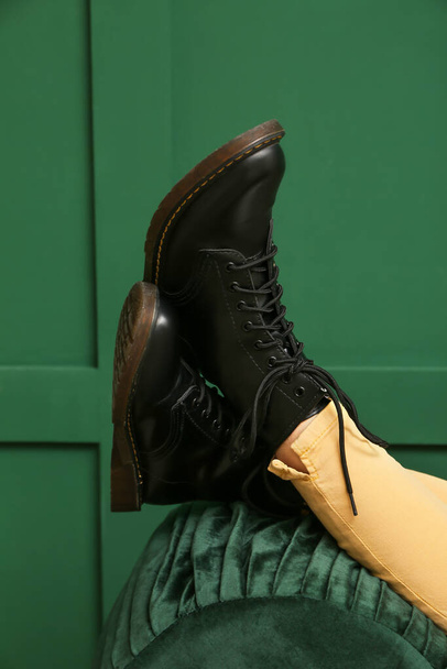 Frauenbeine in schwarzen Stiefeln auf Hocker vor grünem Hintergrund - Foto, Bild