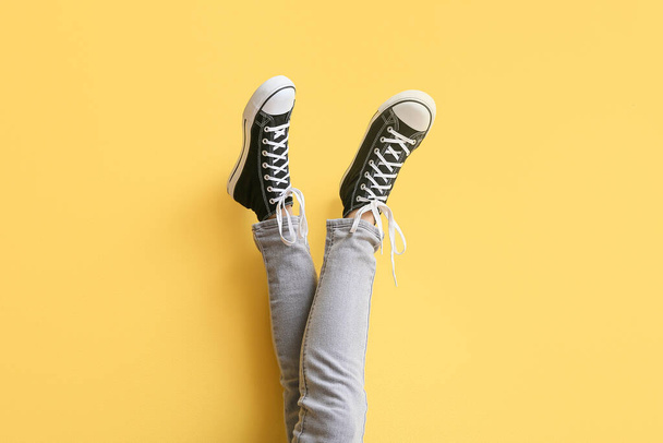 Ноги женщины в черных кроссовках с белыми шнурками на желтом фоне - Фото, изображение