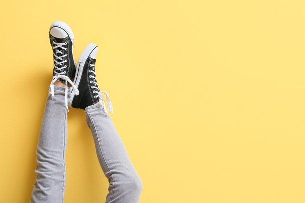 Legs of woman in black sneakers with white laces on yellow background - 写真・画像
