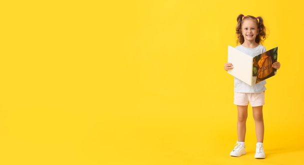 Adorable little girl with book on yellow background - Photo, Image