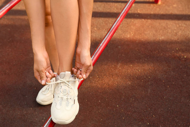 Nainen valkoisissa lenkkarit sitominen nauhoja urheilukentällä, lähikuva - Valokuva, kuva