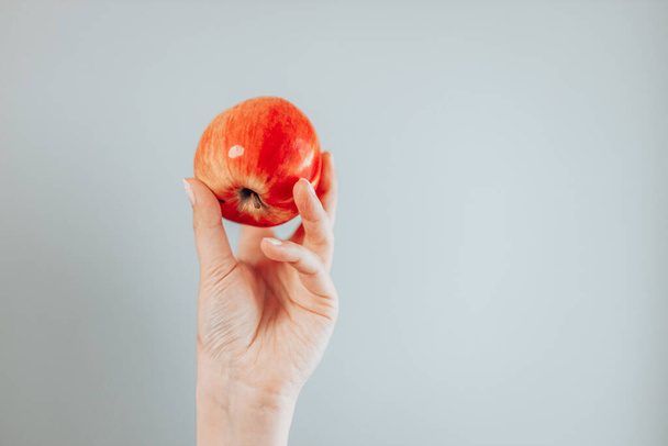 mano sosteniendo manzana roja, aislada sobre un fondo gris. - Foto, Imagen