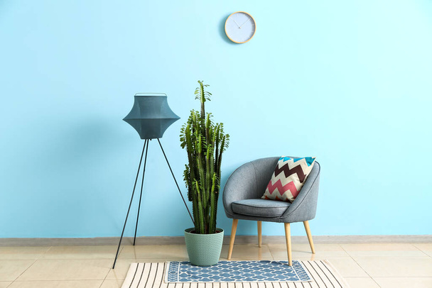 Зеленый кактус с лампой и уютное кресло возле синей стены - Фото, изображение