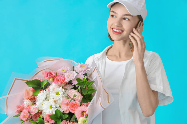 Female courier with bouquet of flowers talking by phone on color background - Foto, afbeelding