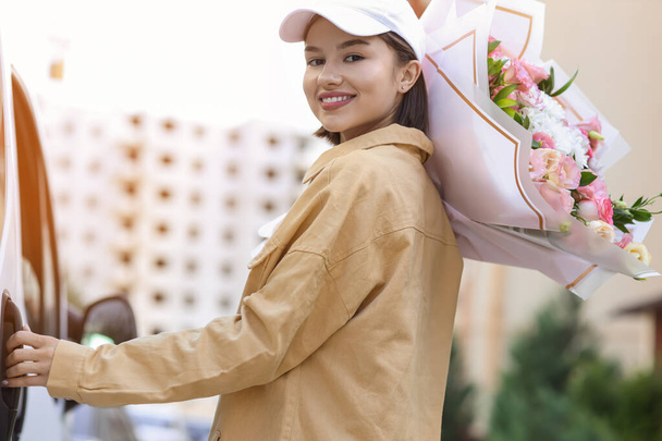 Female courier with bouquet of flowers near car outdoors - Zdjęcie, obraz