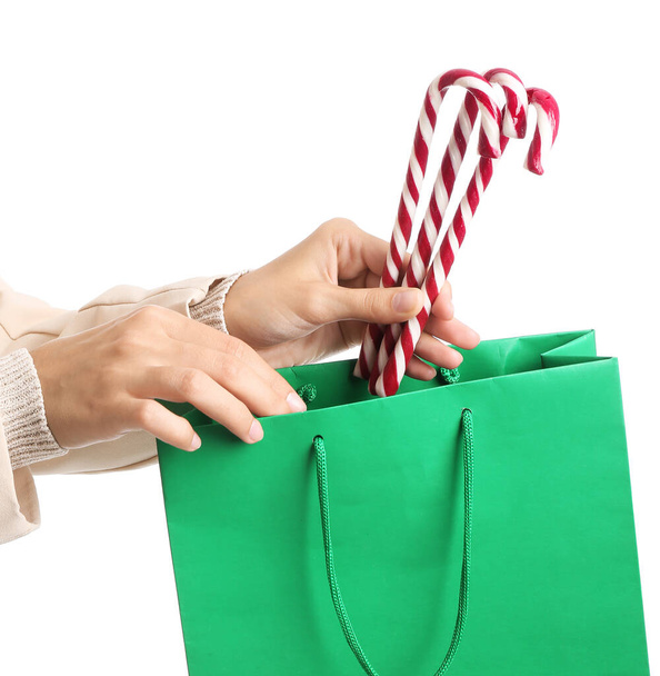 Hands of woman with candy canes and shopping bags on white background - Foto, afbeelding