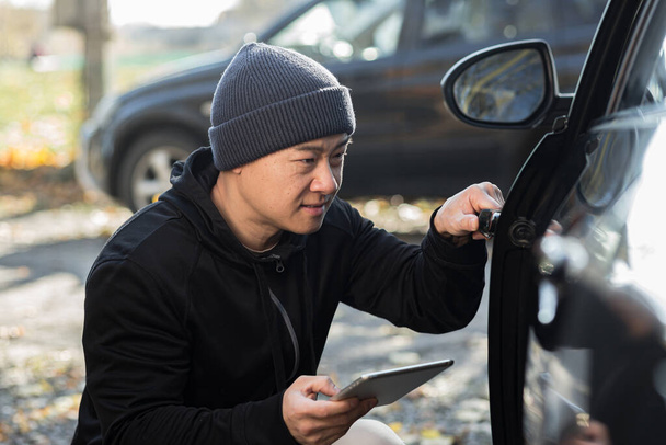 male bandit thief car thief asian uses a tablet to turn off the car alarm - Fotoğraf, Görsel