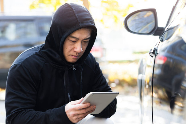 male bandit thief car thief asian uses a tablet to turn off the car alarm - Foto, imagen